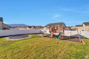Fenced backyard with a residential view, a trampoline, and a playground