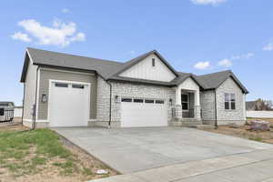 View of front of house with stone siding, an attached garage, a shingled roof, and driveway