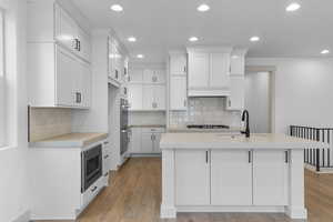 Kitchen featuring recessed lighting, tasteful backsplash, white cabinetry, light wood-style flooring, and a center island with sink