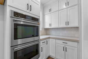 Kitchen with double oven, white cabinets, light countertops, and decorative backsplash