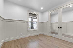 Empty room featuring a decorative wall, a wainscoted wall, light wood-style floors, french doors, and recessed lighting