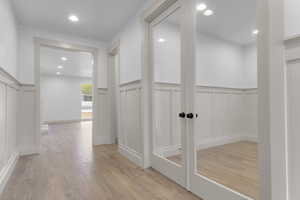 Hall with a wainscoted wall, a decorative wall, light wood-style flooring, and recessed lighting