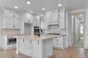 Kitchen with recessed lighting, white cabinets, light countertops, tasteful backsplash, and light wood finished floors