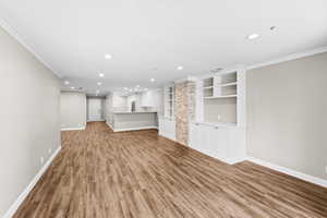 Unfurnished living room with light wood-style floors, crown molding, recessed lighting, and built in shelves
