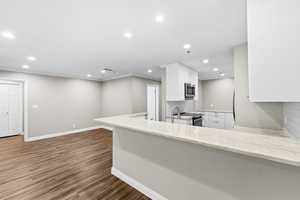 Kitchen featuring white cabinets, light stone countertops, backsplash, recessed lighting, and dark wood finished floors