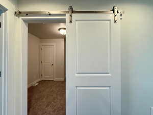 Corridor featuring dark colored carpet and a barn door