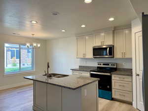 Kitchen with electric range oven, dark stone countertops, stainless steel microwave, light wood finished floors, and a kitchen island with sink