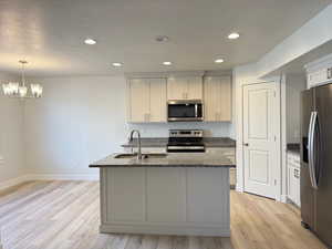 Kitchen with appliances with stainless steel finishes, dark stone counters, recessed lighting, light wood-type flooring, and a center island with sink