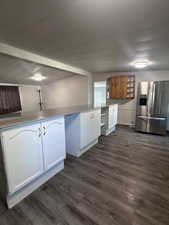 Kitchen with stainless steel fridge, dark wood-style floors, light stone countertops, white cabinetry, and a textured ceiling