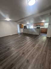 Unfurnished living room featuring a textured ceiling, dark wood-style floors, and plenty of natural light