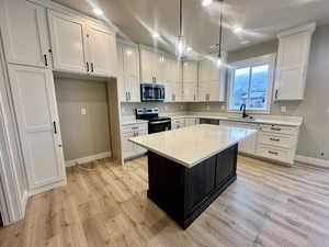 Kitchen with a center island, range with electric stovetop, decorative light fixtures, white cabinetry, and stainless steel microwave