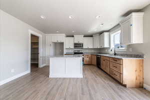 Kitchen featuring white cabinetry, appliances with stainless steel finishes, light wood-style flooring, a kitchen island, and light stone counters