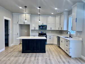 Kitchen with white cabinetry, decorative light fixtures, stainless steel appliances, a center island, and light stone counters