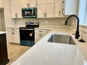Kitchen with appliances with stainless steel finishes, white cabinets, light wood-style flooring, and light stone counters