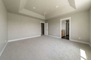 Unfurnished bedroom featuring a tray ceiling, light carpet, and ensuite bathroom