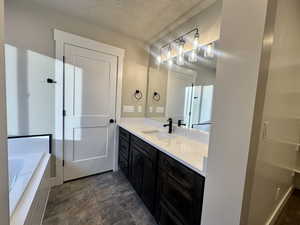 Bathroom with vanity, a relaxing tiled tub, a textured ceiling, and stone finish floors