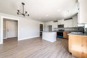 Kitchen with a chandelier, appliances with stainless steel finishes, white cabinets, light wood-type flooring, and light stone counters