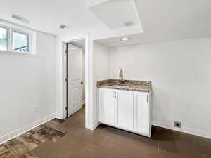 Bar area featuring white cabinets, light stone counters, a textured ceiling, and dark wood finished floors
