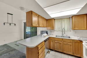 Kitchen featuring a peninsula, brown cabinetry, light countertops, light tile patterned floors, and stainless steel appliances