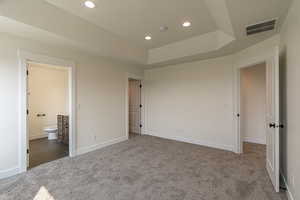 Unfurnished bedroom featuring a raised ceiling, dark colored carpet, recessed lighting, and ensuite bathroom