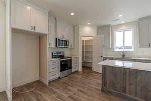 Kitchen with appliances with stainless steel finishes, recessed lighting, light stone counters, and dark wood-type flooring