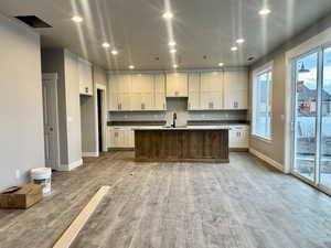 Kitchen featuring recessed lighting, white cabinetry, a kitchen island with sink, light wood-style flooring, and dark stone counters