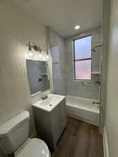 Full bathroom with a textured wall, vanity, dark wood-style floors, and shower / bathtub combination