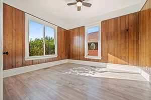 Unfurnished room featuring wooden walls, wood finished floors, and a ceiling fan
