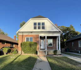 View of front facade with a front yard, a porch, and brick siding