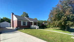 View of front facade featuring an outbuilding, brick siding, a chimney, a front yard, and a detached garage