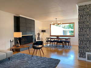 Living room with wood finished floors, a chandelier, a textured ceiling, a fireplace, and crown molding