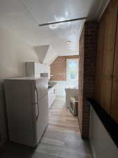 Kitchen with brick wall, white cabinetry, freestanding refrigerator, light wood finished floors, and lofted ceiling