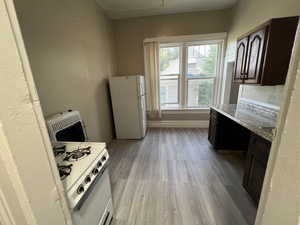 Kitchen featuring dark brown cabinetry, white appliances, light wood finished floors, heating unit, and a desk