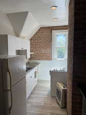 Kitchen featuring brick wall, white cabinets, white appliances, lofted ceiling, and light wood finished floors