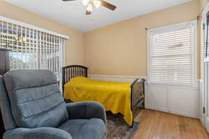 Bedroom featuring a decorative wall, hardwood / wood-style floors, a wainscoted wall, and ceiling fan