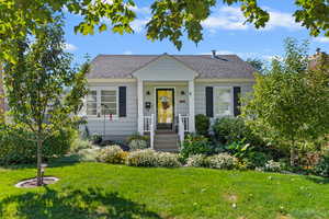 Bungalow-style home featuring roof with shingles, a front lawn, and covered porch