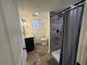 Bathroom featuring vanity, a textured ceiling, a stall shower, and dark stone finish floors