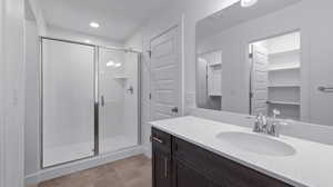 Bathroom featuring a shower stall, vanity, a spacious closet, and recessed lighting