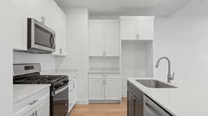 Kitchen featuring appliances with stainless steel finishes, white cabinetry, light wood-type flooring, and light stone counters