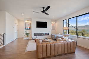 Living room with wood finished floors, recessed lighting, a glass covered fireplace, and ceiling fan