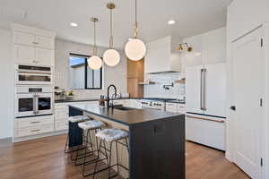 Kitchen featuring an island with sink, premium appliances, a breakfast bar, decorative light fixtures, and tasteful backsplash