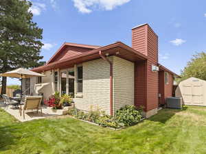 View of side of property featuring a chimney, a storage unit, a yard, a patio area, and brick siding