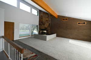 Living room with plenty of natural light, beam ceiling, a stone fireplace, brick wall, and high vaulted ceiling