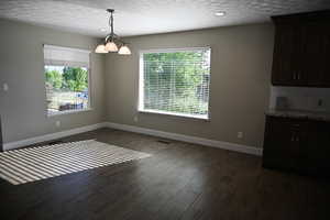 Unfurnished dining area featuring a textured ceiling, dark wood-type flooring, a chandelier, and recessed lighting