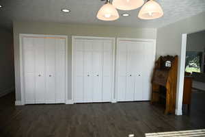 Unfurnished bedroom with two closets, dark wood-style flooring, recessed lighting, and a textured ceiling
