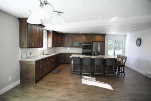 Kitchen featuring dark brown cabinets, tasteful backsplash, decorative light fixtures, appliances with stainless steel finishes, and light stone counters