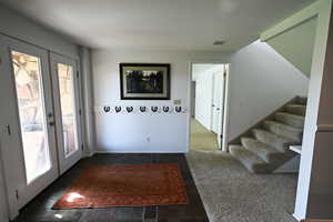 Foyer entrance with stairs, french doors, and dark colored carpet
