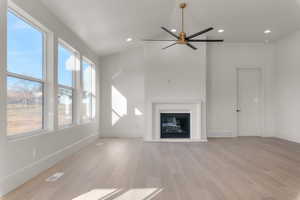 Unfurnished living room featuring ceiling fan, light wood-style floors, a glass covered fireplace, recessed lighting, and vaulted ceiling