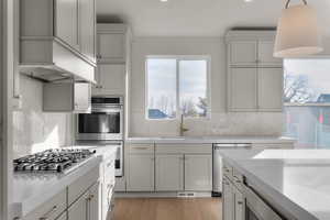 Kitchen featuring light wood finished floors, stainless steel appliances, pendant lighting, light stone counters, and decorative backsplash