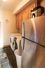 Laundry area featuring stone tile floors, washer and clothes dryer, and cabinet space